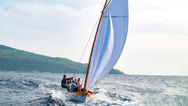 A sailer leans over the yacht's side whilst it's sailing.