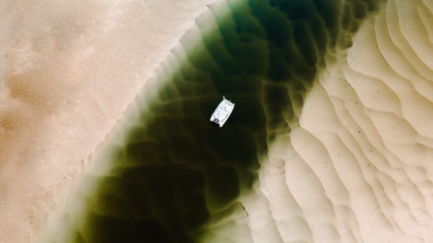 Aerial shot of the yacht in between two sandbanks on a green-water river.