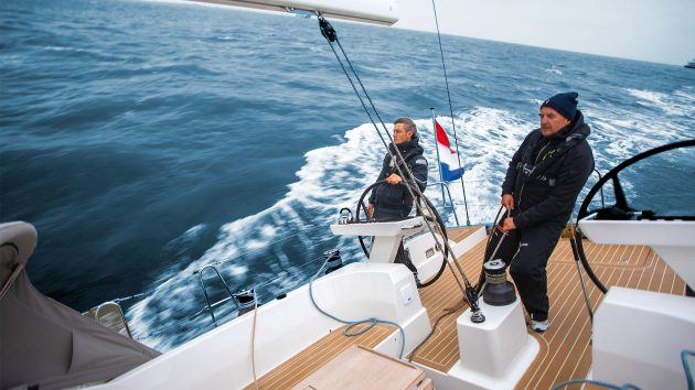 Two people standing on a yaht deck and holding sailing equipment 